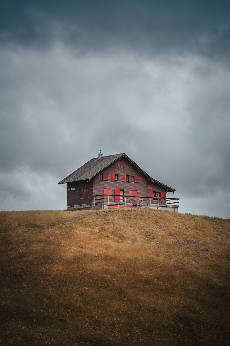 A red house sitting on top of a hill under a cloudy sky